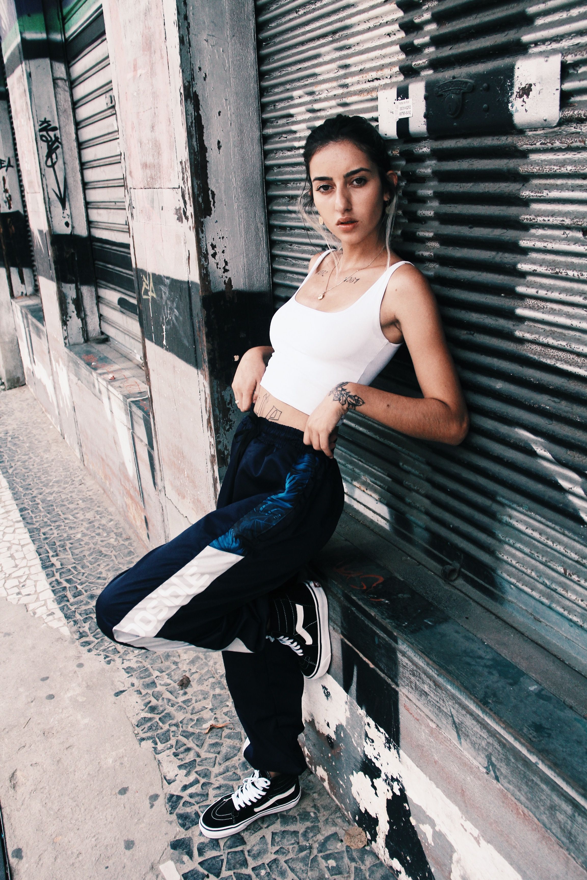 Young woman in fashionable urban attire posing confidently against a corrugated metal wall outdoors.