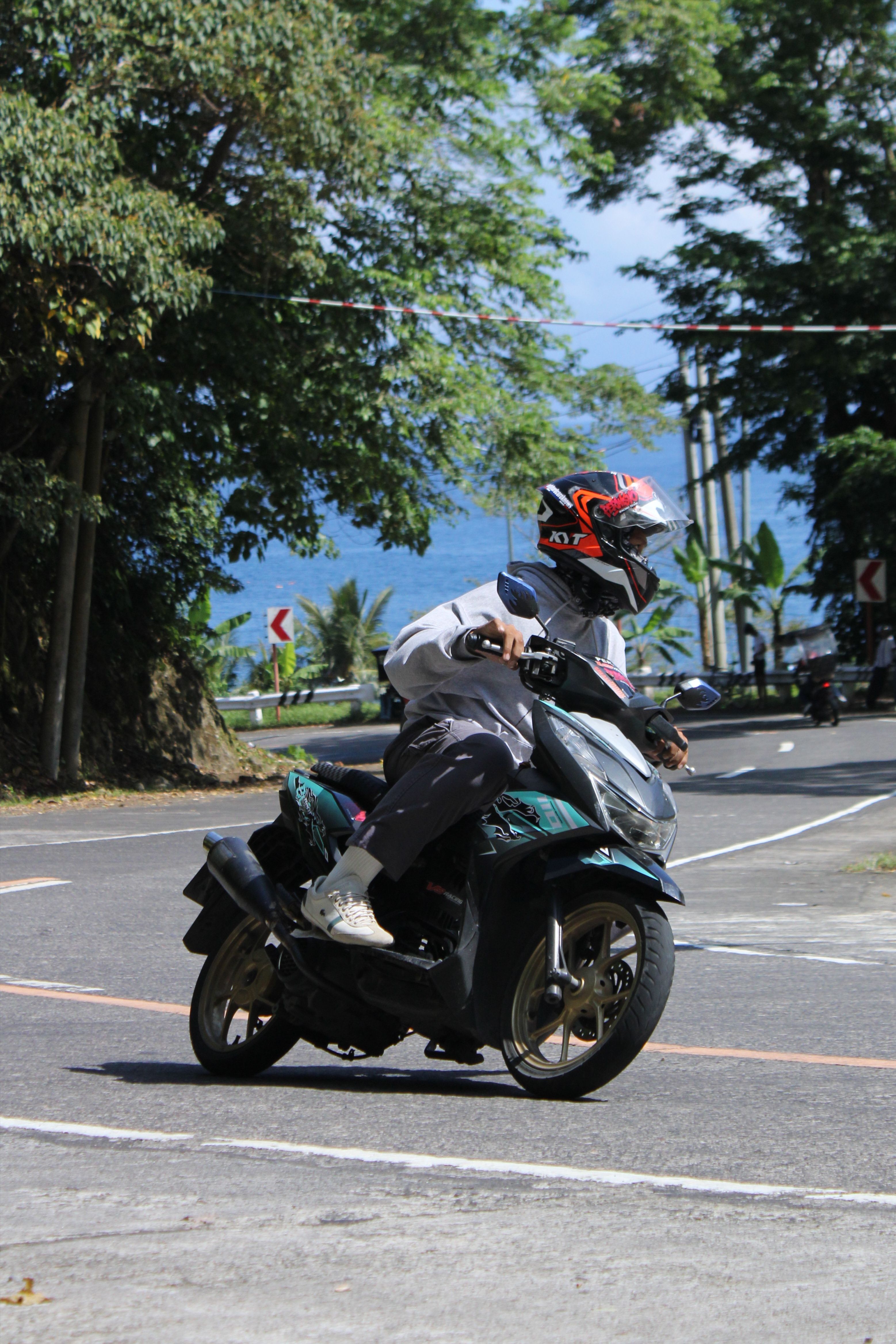 Tourist wearing a full-face helmet riding a scooter along a coastal road in Bali during daytime
