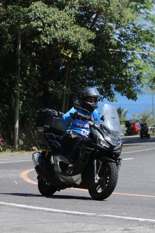 Free Motorcyclist navigating a scenic curve on a sunny day, wearing full gear for safety. Stock Photo