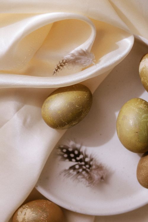 Free A stylish composition of golden Easter eggs on a soft white silk fabric accented with delicate feathers. Stock Photo
