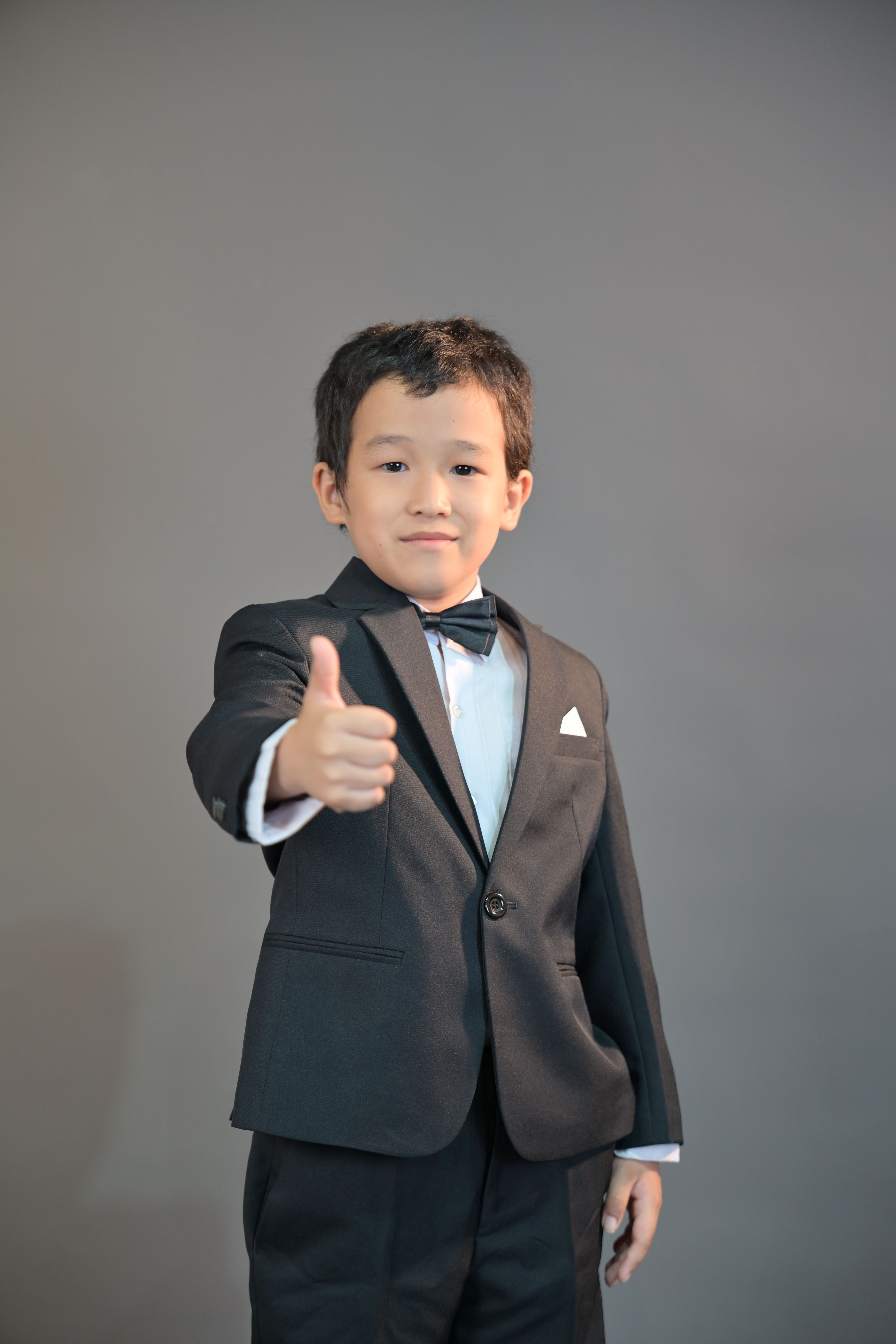 Young boy in a suit and bow tie giving a thumbs up gesture with a confident smile.