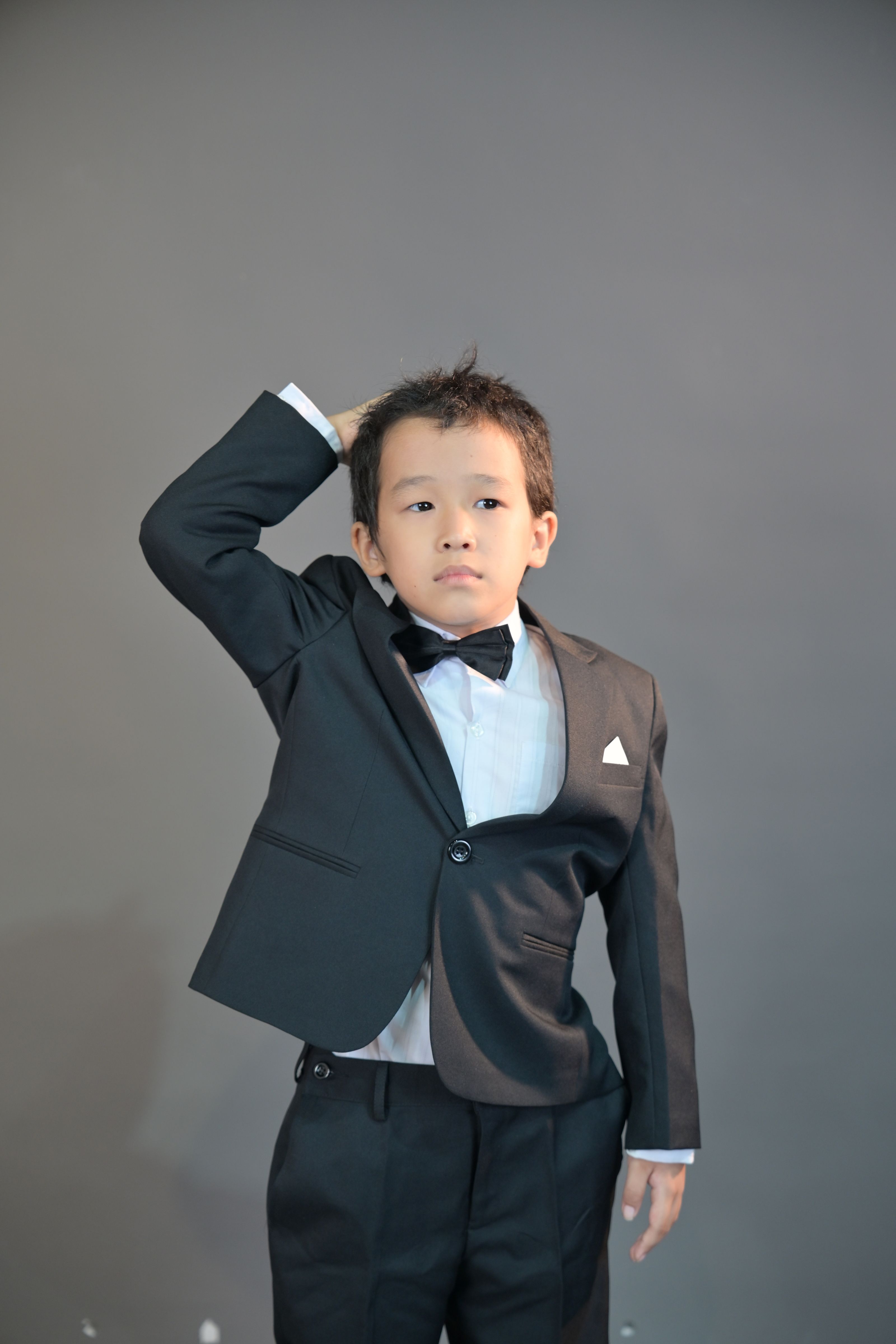 Um menino posando em um terno preto formal com gravata borboleta, em um ambiente interno.