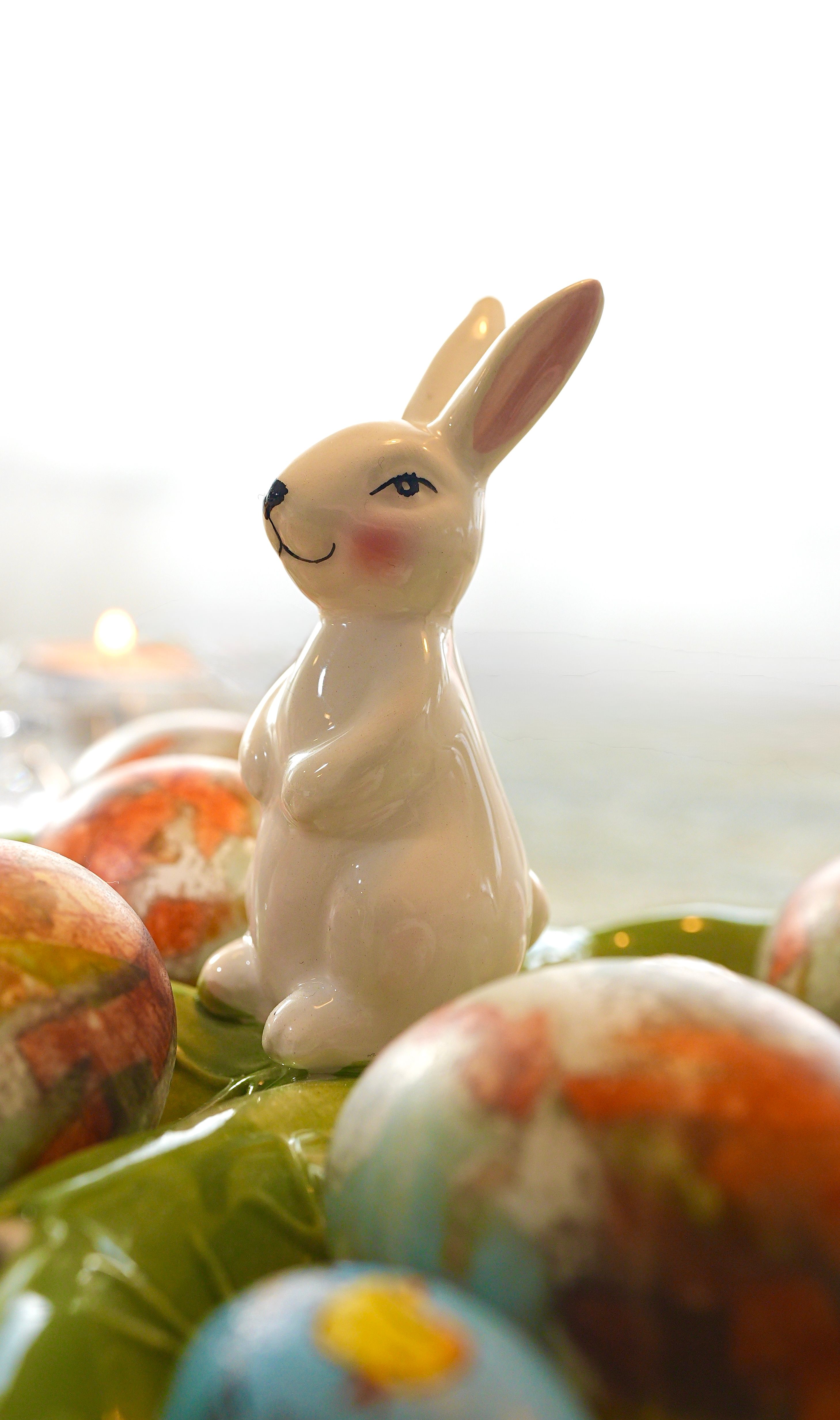 Adorable ceramic bunny figurine surrounded by vibrant, painted Easter eggs on a bright background.