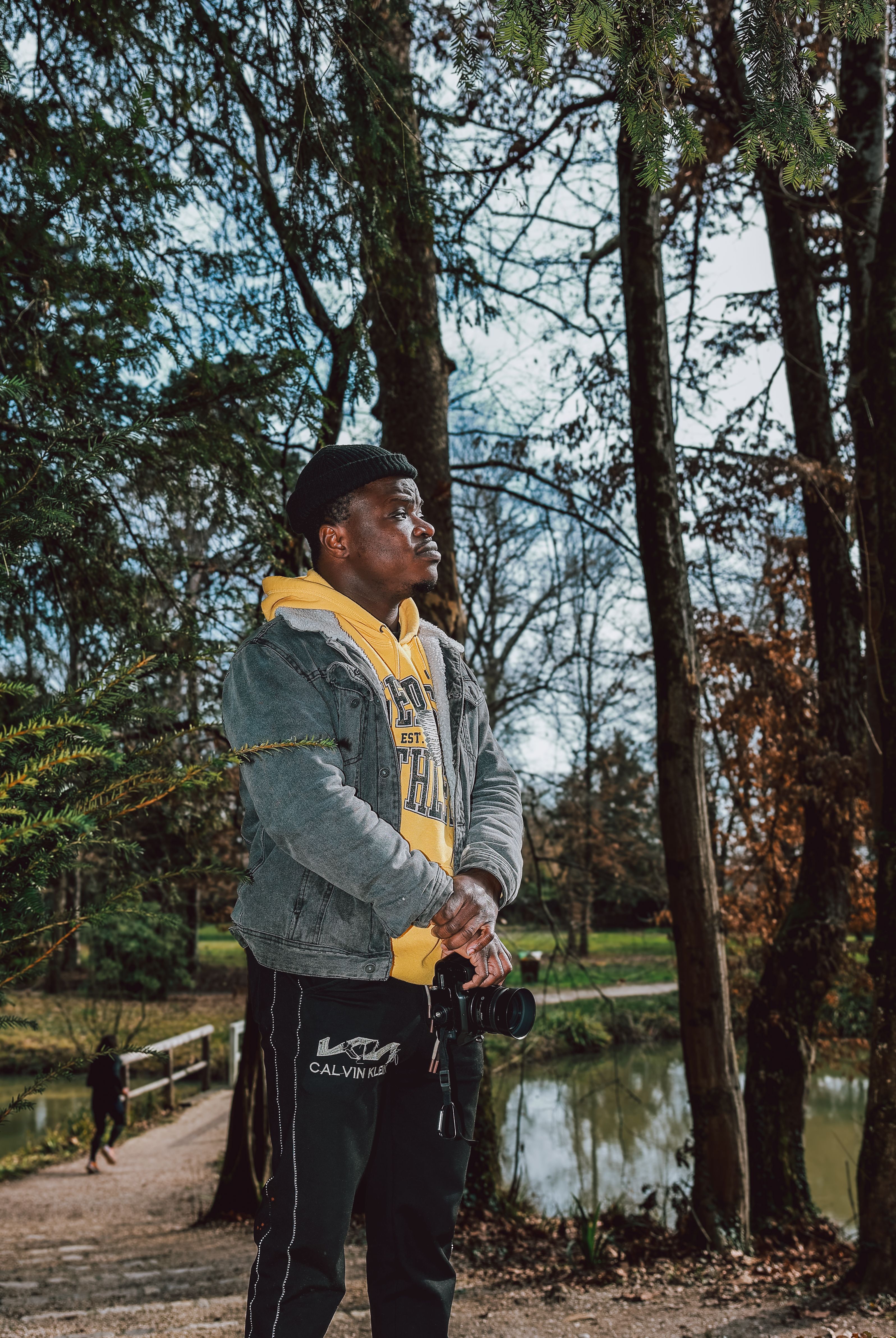 A young man enjoys a walk in the park, holding a camera amidst autumn trees.