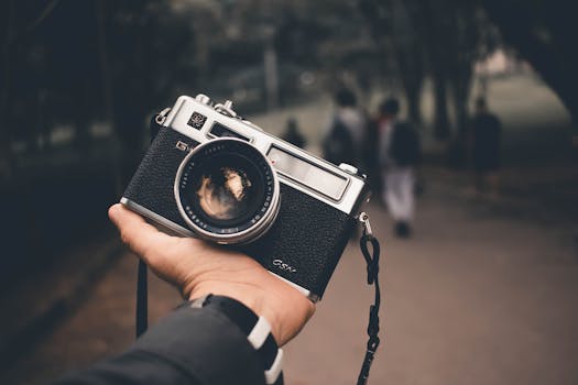 Close-up of a hand holding a vintage analog camera with people blurred in the background.