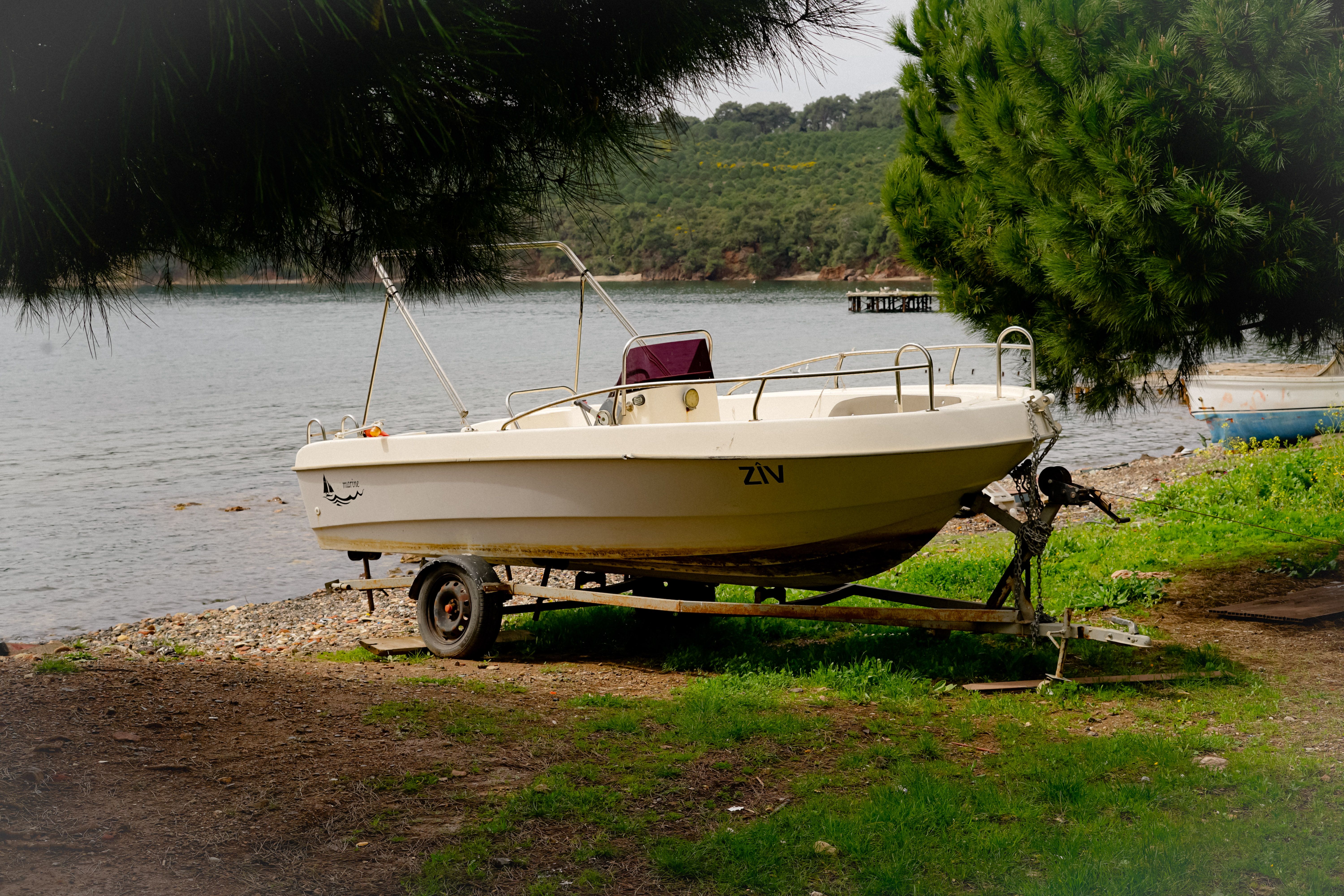 A small boat on a trailer beside a calm lakeside, showing the sort of manageable trailer package that makes solo launching less intimidating.