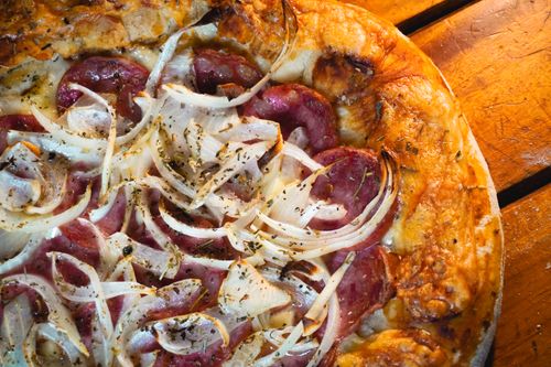 Free Close-up of a rustic pizza topped with fresh onions and salami, perfect for food enthusiasts. Stock Photo