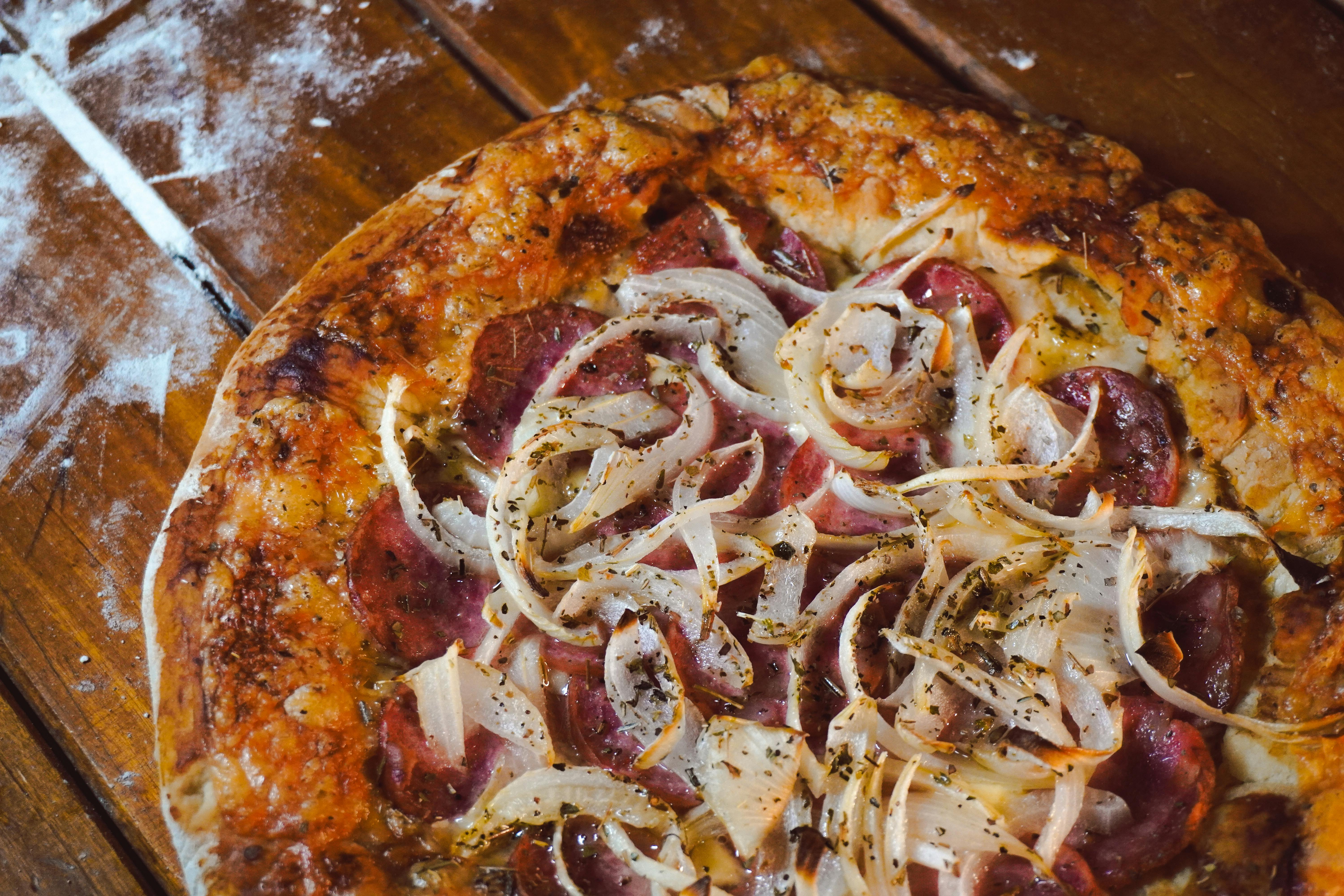 Tasty homemade pepperoni pizza topped with onions and herbs on a rustic wooden table.