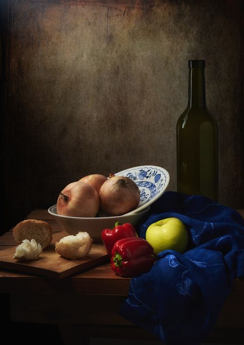 Free A traditional still life featuring onions, peppers, an apple, bread, and a bottle on a wooden table. Stock Photo