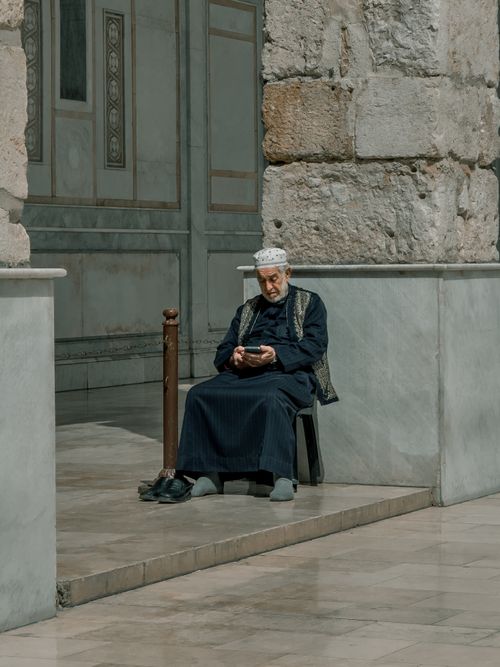 Free An elderly man in traditional clothing sits near a historic mosque in Damascus, Syria. Stock Photo