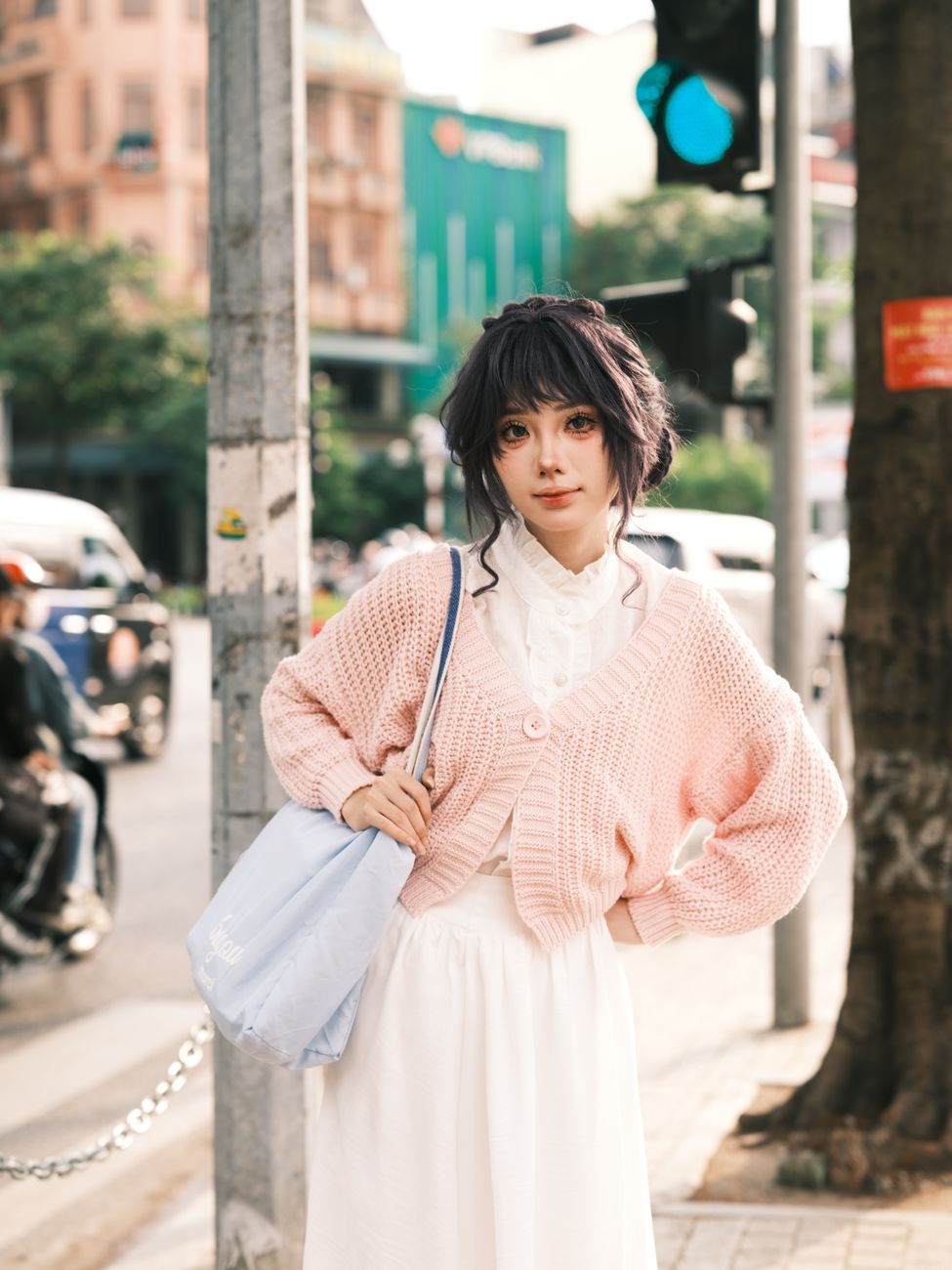 Stylish young woman poses confidently in a bustling city street wearing a pink sweater.