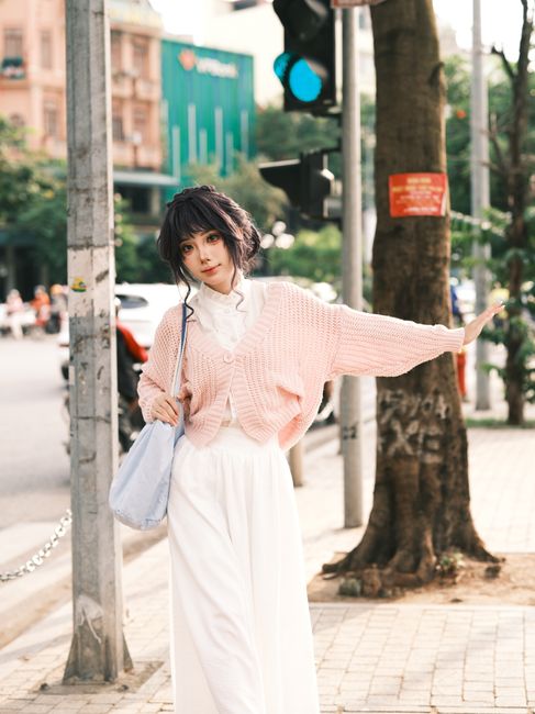 Stylish woman in pink sweater poses confidently at a bustling city intersection.