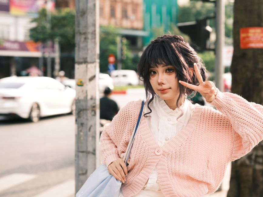 Young woman in pink sweater posing with peace sign on urban street