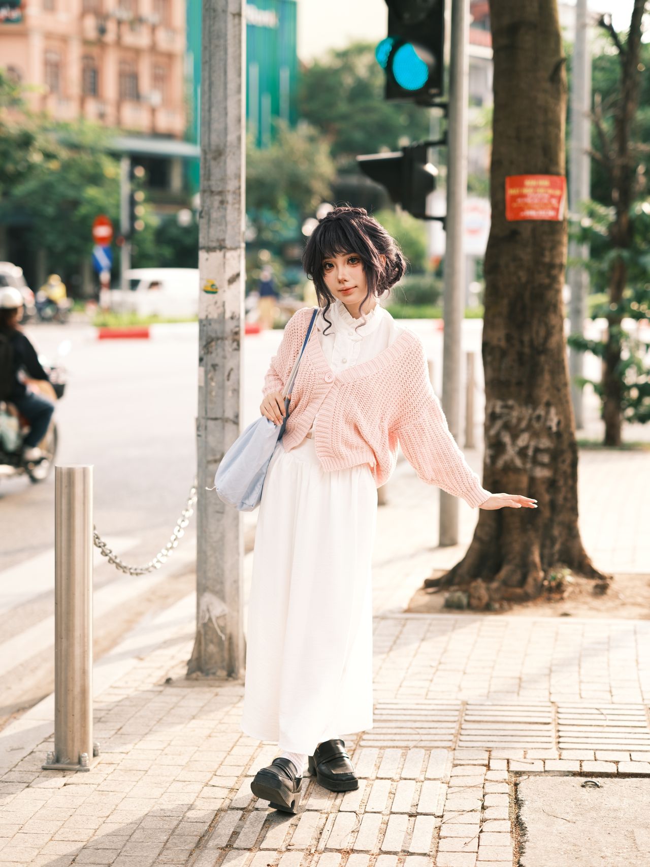 Woman in a pastel pink knit sweater and white skirt on a city street