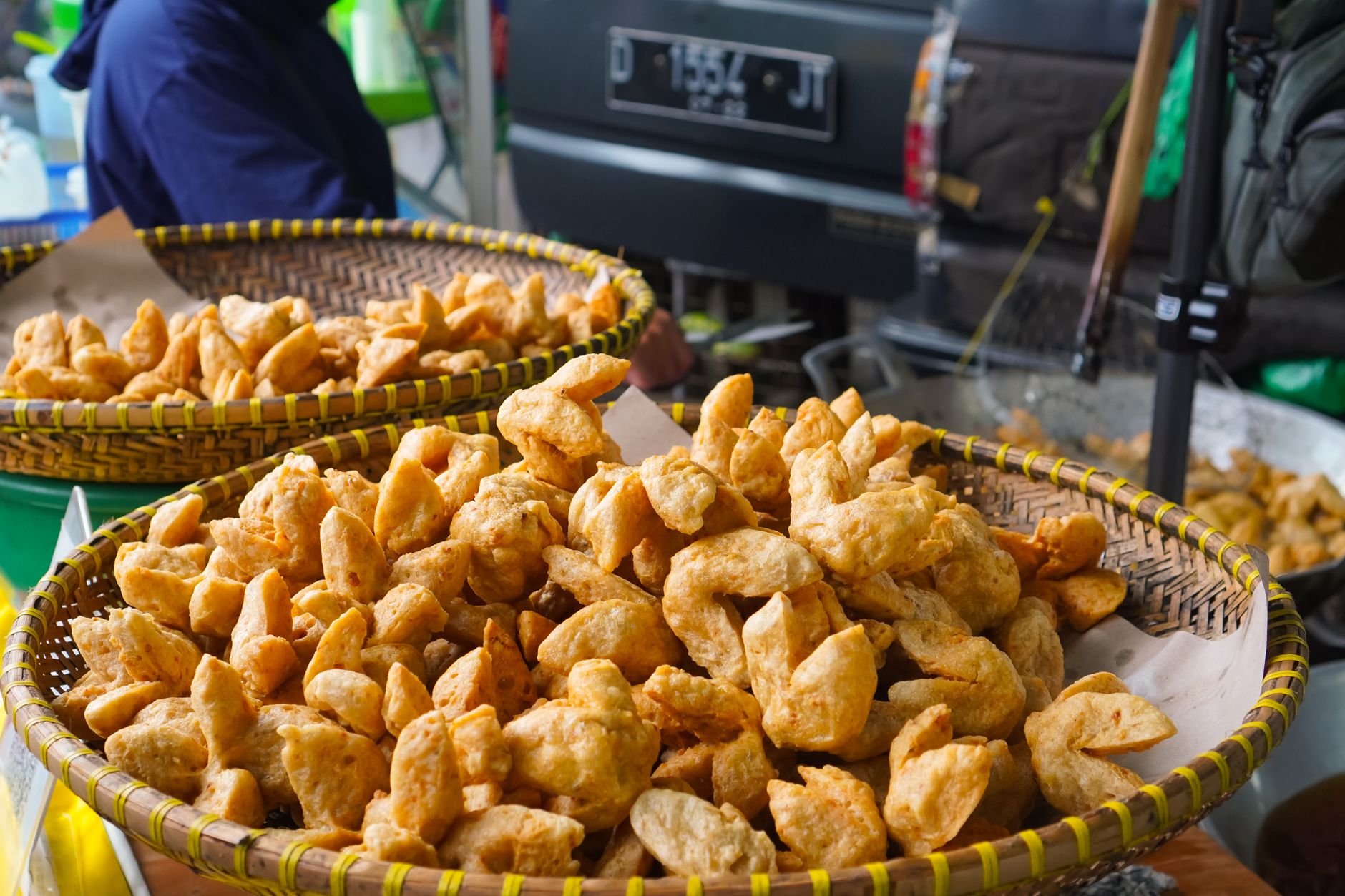 Close-up of crispy fried snacks in woven baskets at a bustling street market.