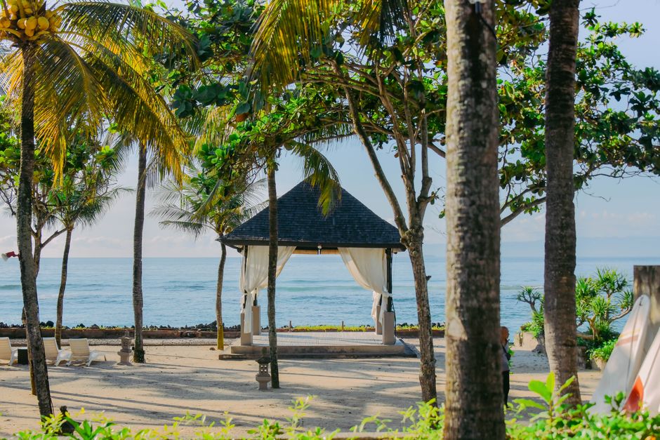 Tropical pavilion with palm trees by the beach in Bali, Indonesia, offering a serene coastal view.