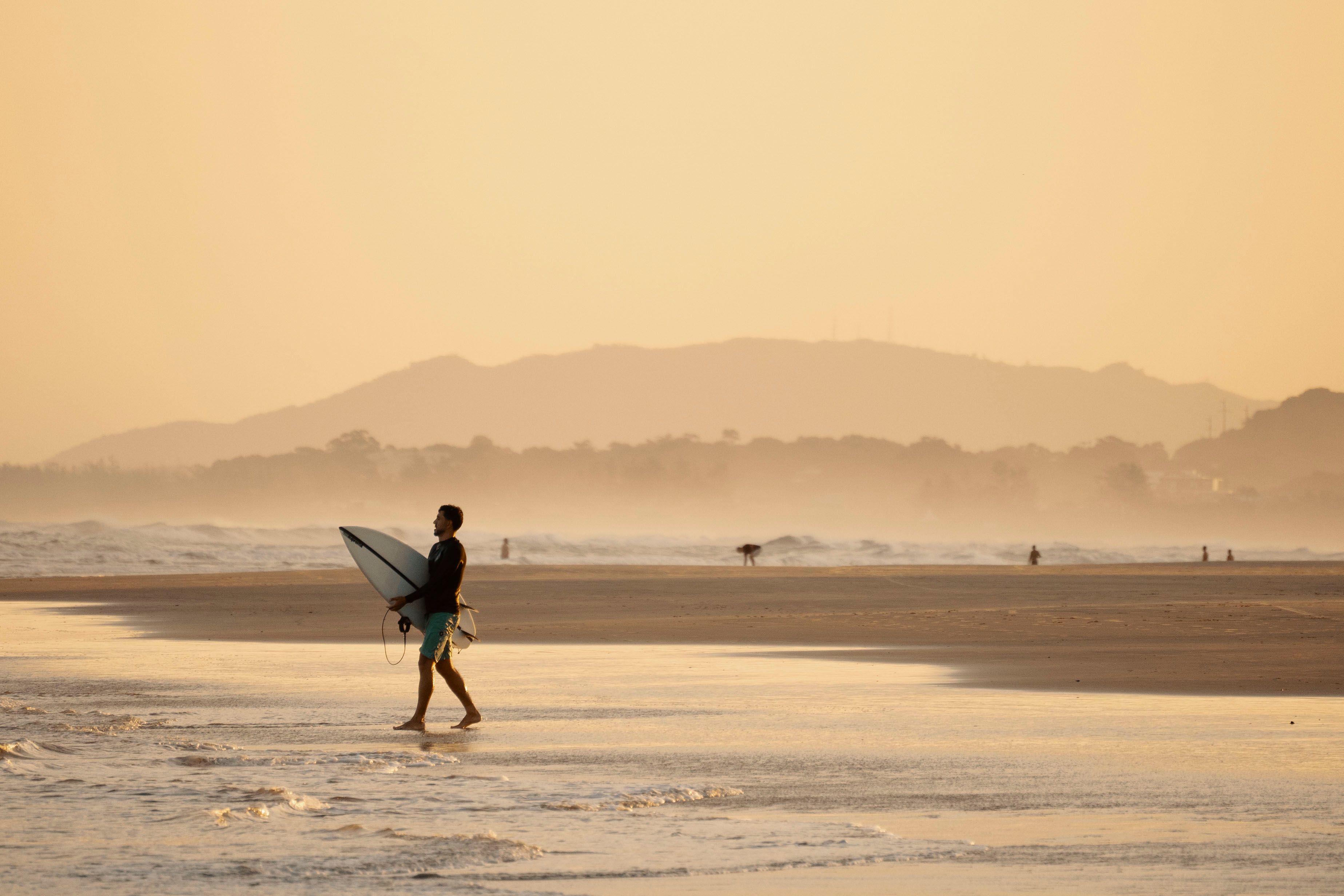 Woman Holding Surf Board Standing on Shoreline during Sunset