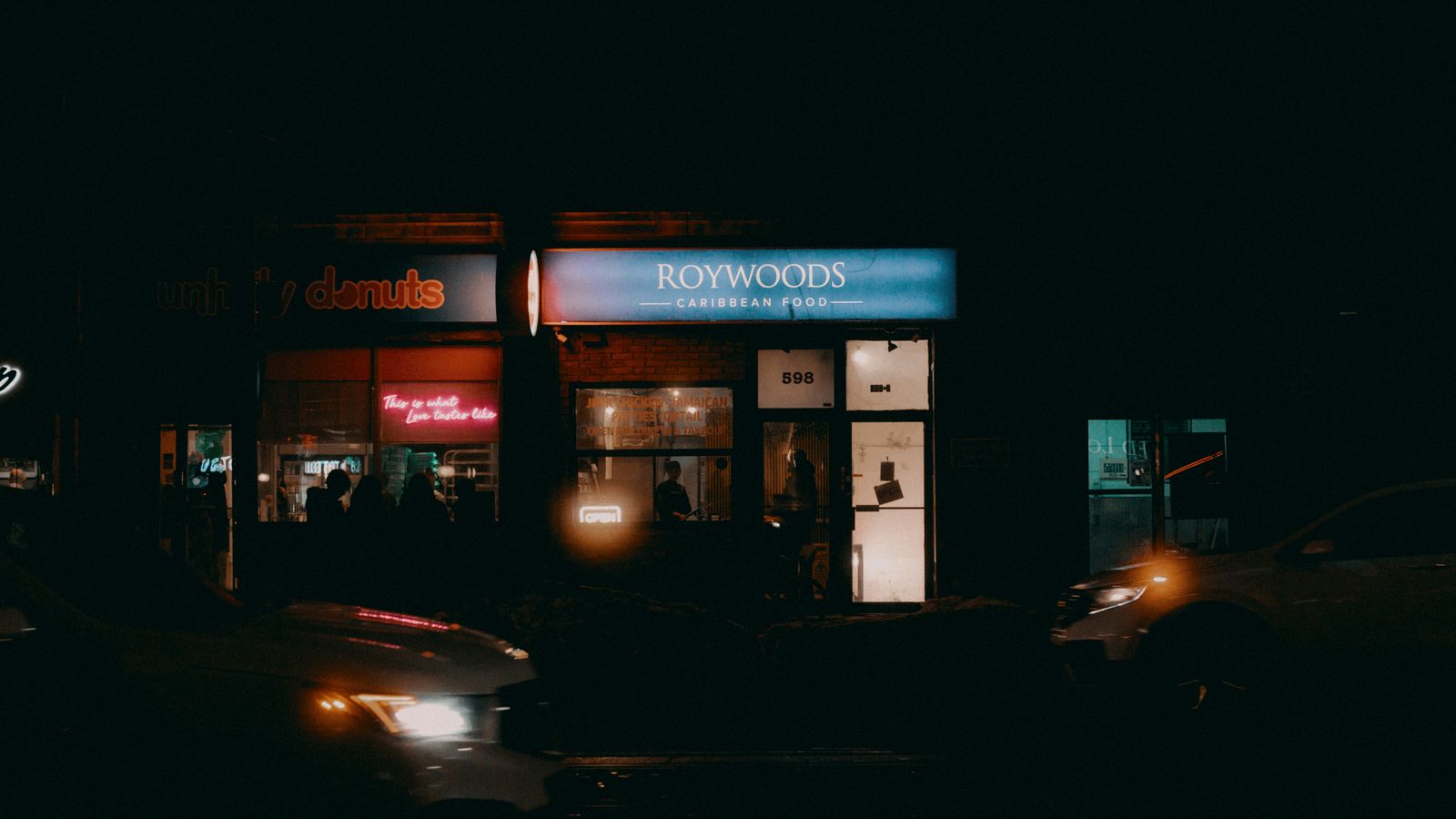 A vibrant nighttime view of a street with illuminated shopfronts and neon signs.
