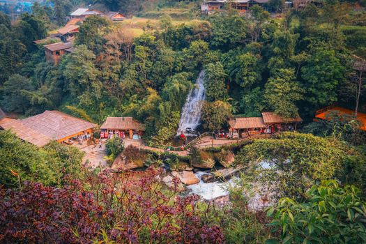 Aerial view of waterfall and houses surrounded by lush greenery in Sa Pa, Vietnam.