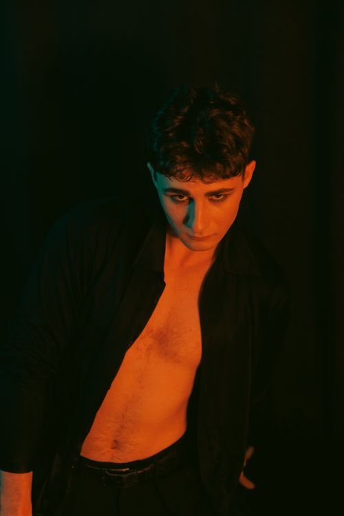 Free A young man in dramatic lighting poses with an introspective expression, showcasing mood and contrast. Stock Photo