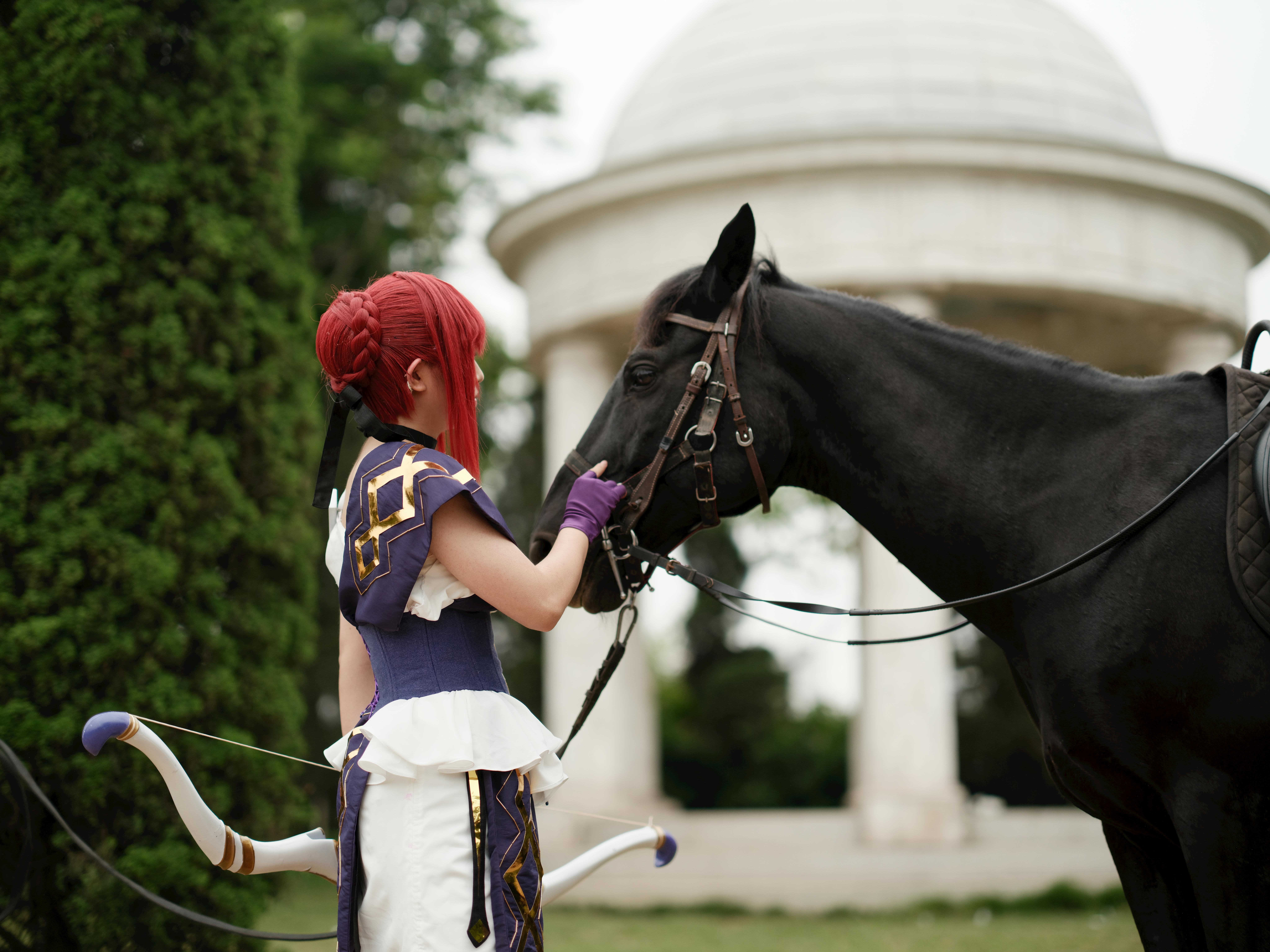 A cosplayer dressed in vibrant attire stands beside a horse in a lush garden with a classical dome backdrop.