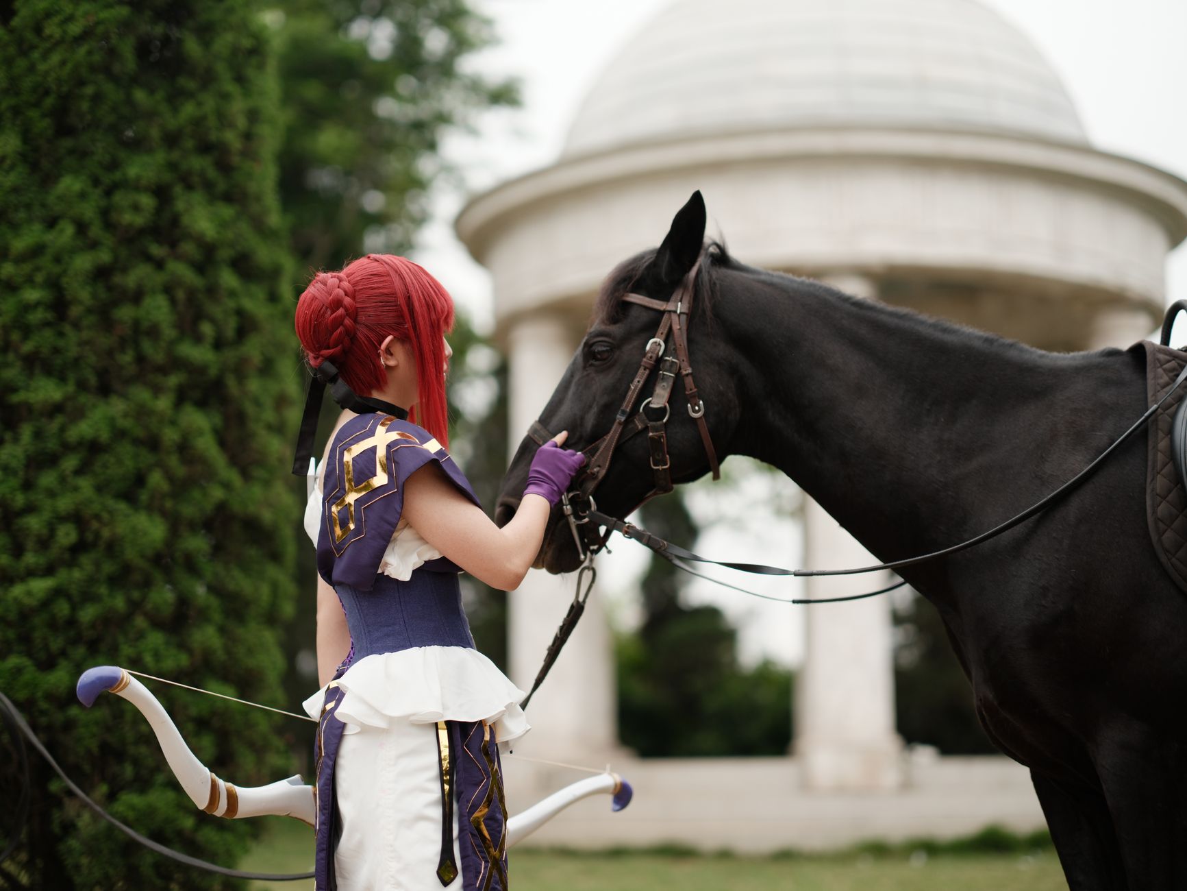 A cosplayer dressed in vibrant attire stands beside a horse in a lush garden with a classical dome backdrop.