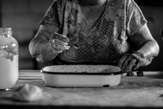 Black and white photo of a senior woman baking cookies, emphasizing traditional cooking.