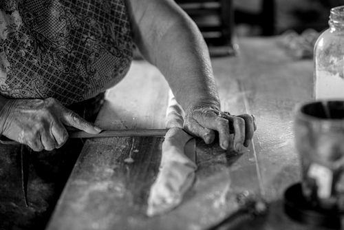 Free A close-up shot of hands rolling dough on a wooden table in a rustic kitchen setting, black and white. Stock Photo