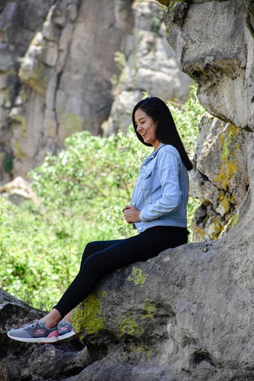 Woman in Blue Denim Long Sleeve Sitting on Rock