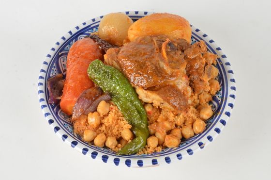 Couscous topped with braised lamb, chickpeas, green chili, carrot and potatoes in a patterned bowl
