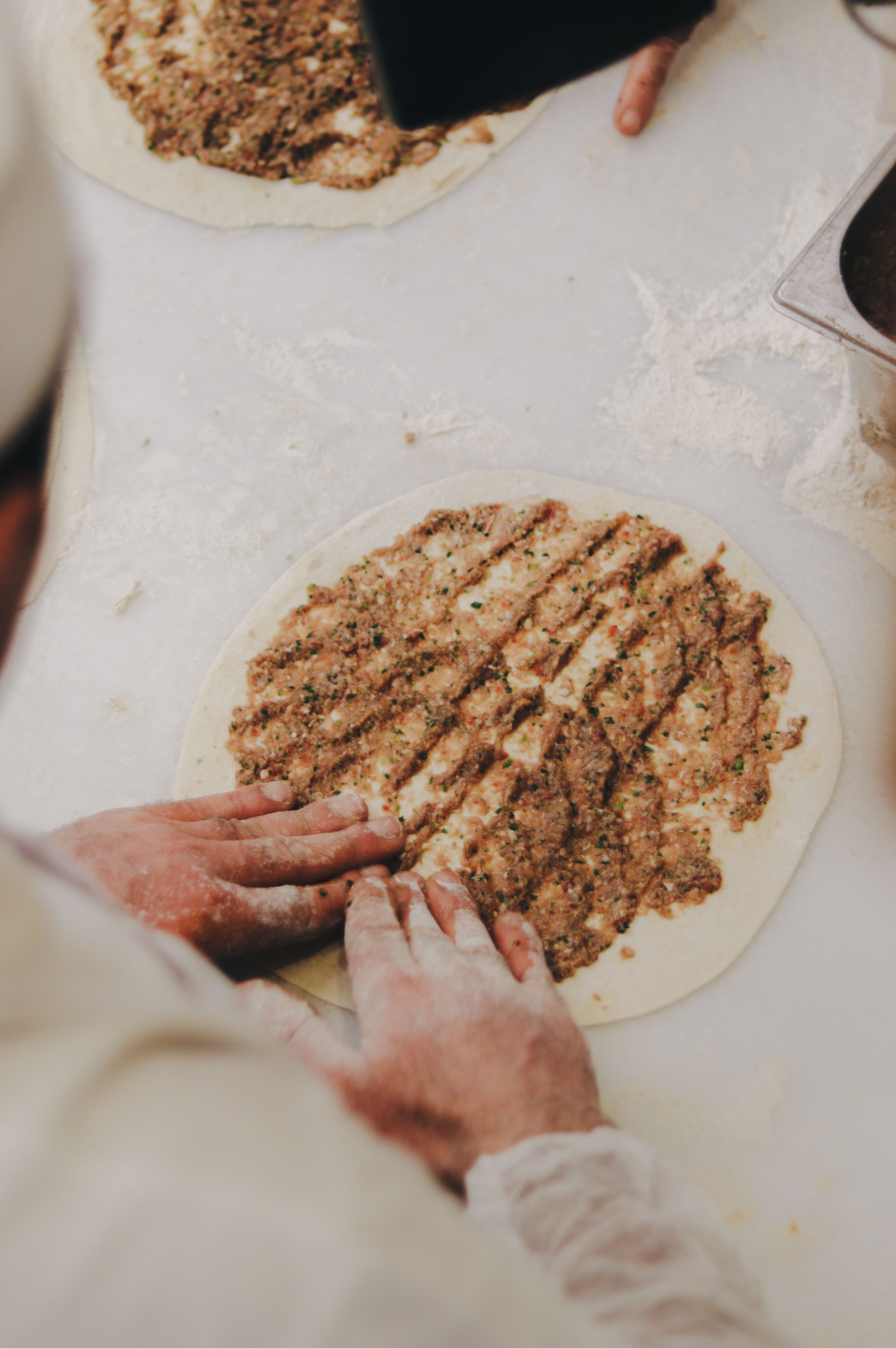 Mains farinées d’un cuisinier étalant la garniture de viande hachée et de persil sur une pâte ronde de lahmacun