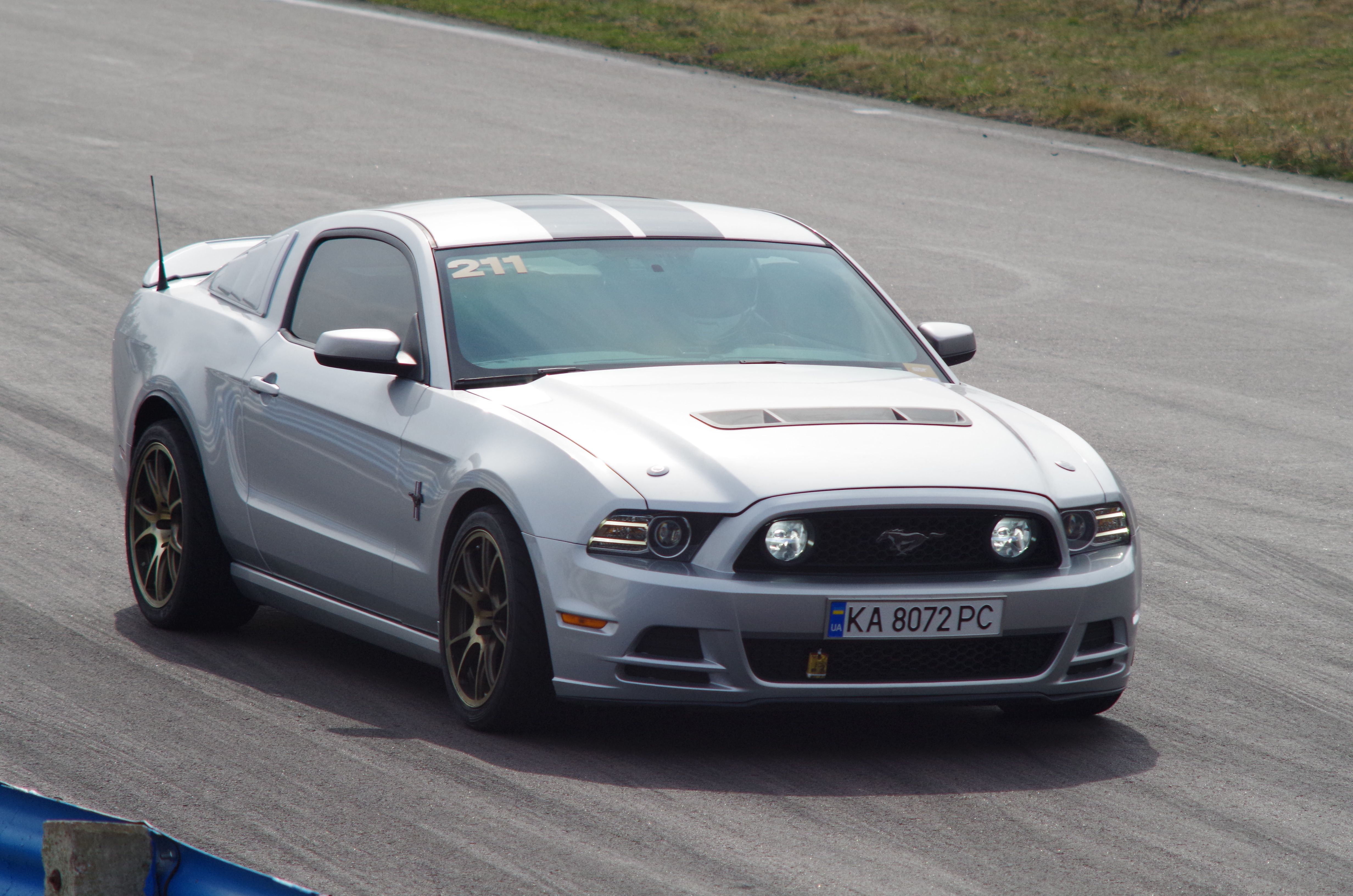 A sleek silver Ford Mustang races on a track during the day in Kyiv, Ukraine.