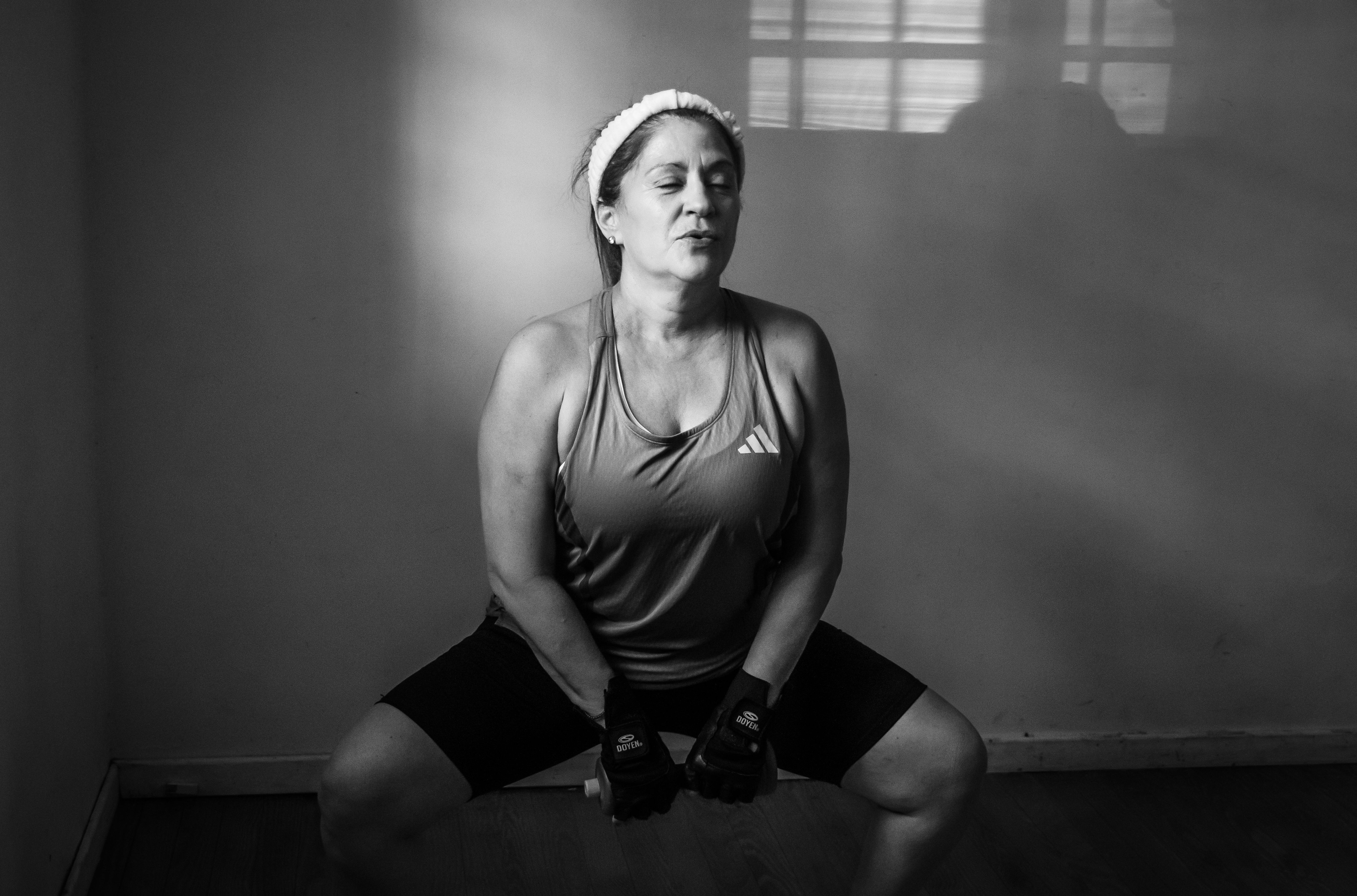 Black and white photo of a female athlete doing squats indoors, emphasizing focus and determination.