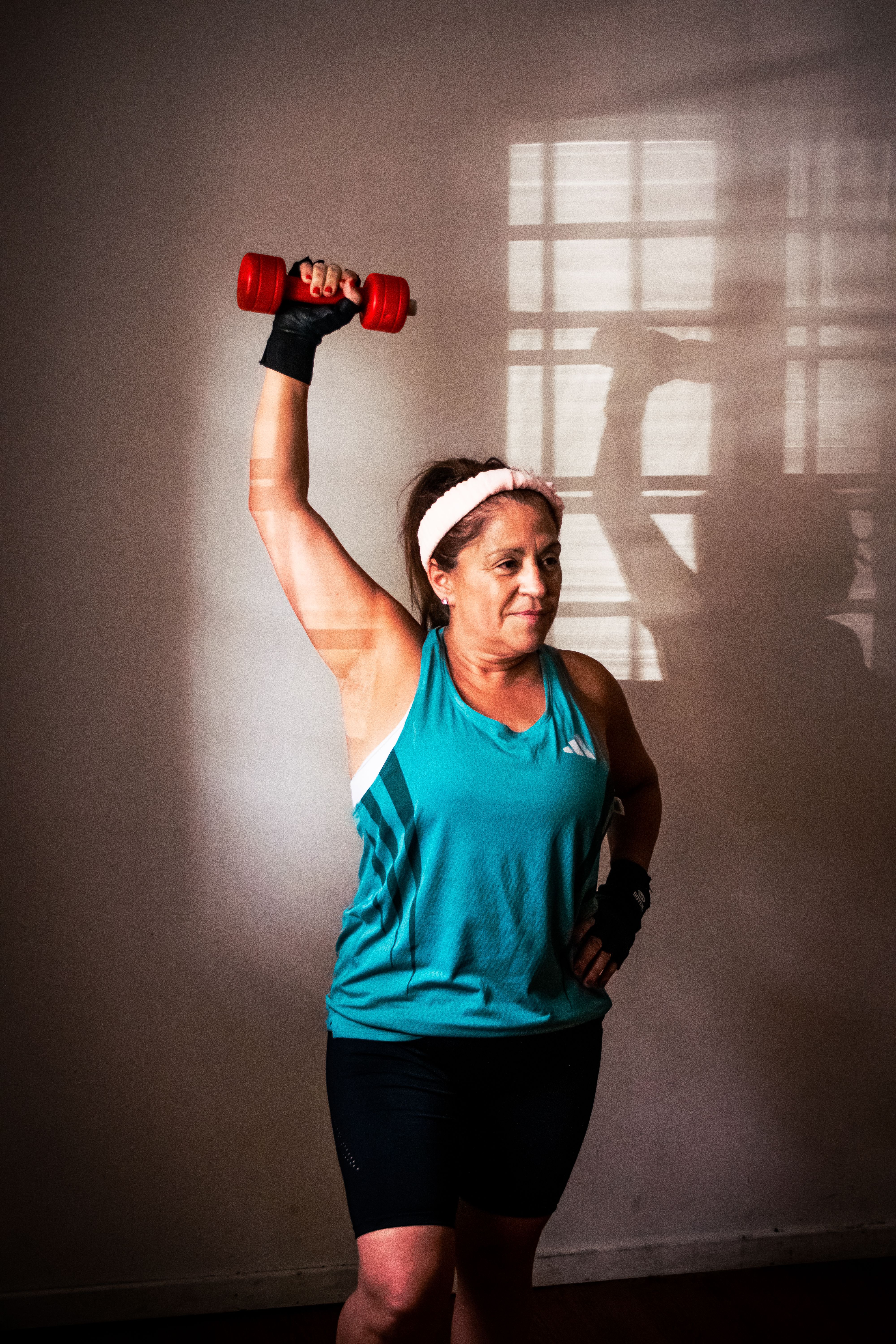 Middle-aged woman lifting a red dumbbell indoors, demonstrating strength and fitness at home.