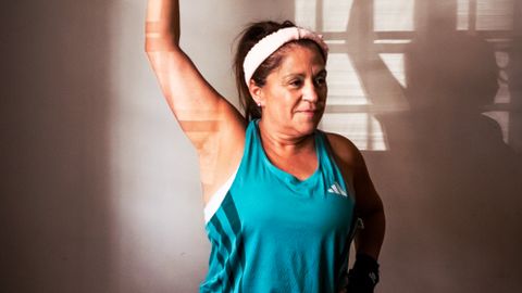 Middle-aged woman lifting a red dumbbell indoors, demonstrating strength and fitness at home.