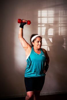 Middle-aged woman lifting a red dumbbell indoors, demonstrating strength and fitness at home.