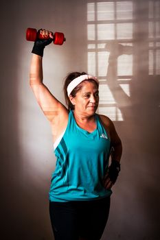 Confident senior woman lifting a dumbbell indoors, showcasing strength and fitness.