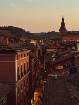 View of a historic street lined with buildings and a church spire at sunset in Bologna, Italy.