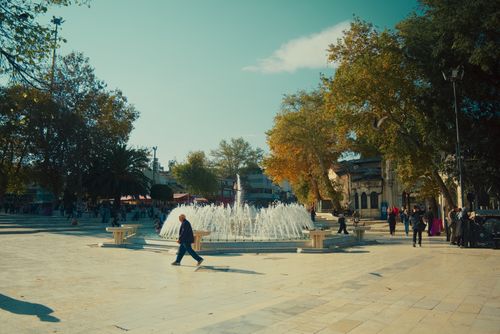 Free A vibrant city square with a central fountain surrounded by people on a sunny day. Stock Photo