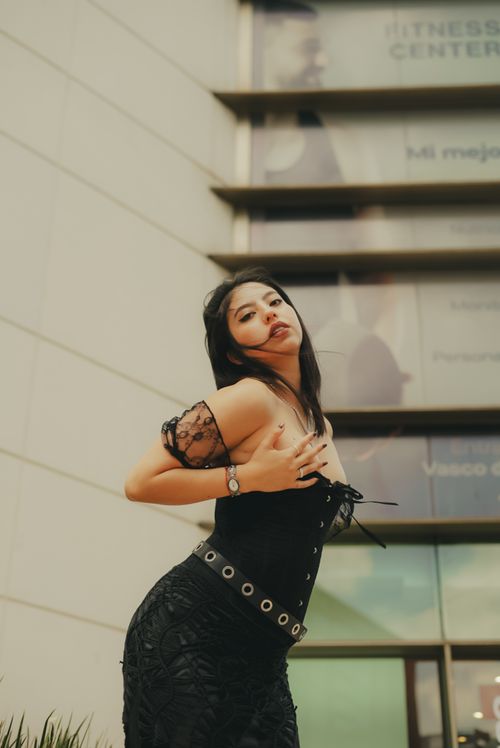 Free Chic woman in black dress poses confidently outside a modern fitness center. Stock Photo