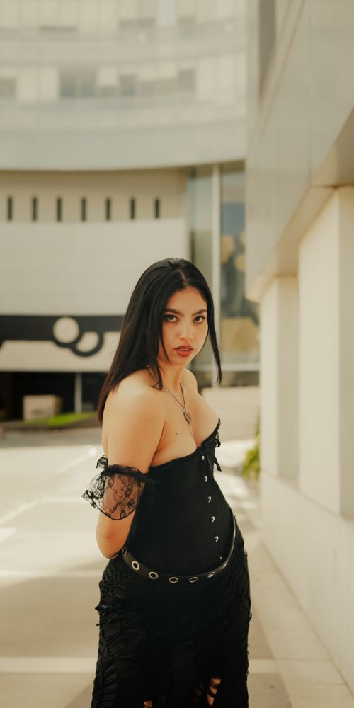 Free Fashionable woman in black lace dress poses confidently in urban setting. Bright day captures trendy style. Stock Photo