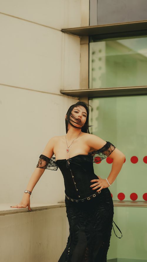Free Stylish woman poses in a black gothic dress against modern architecture. Fashionable and dramatic look. Stock Photo