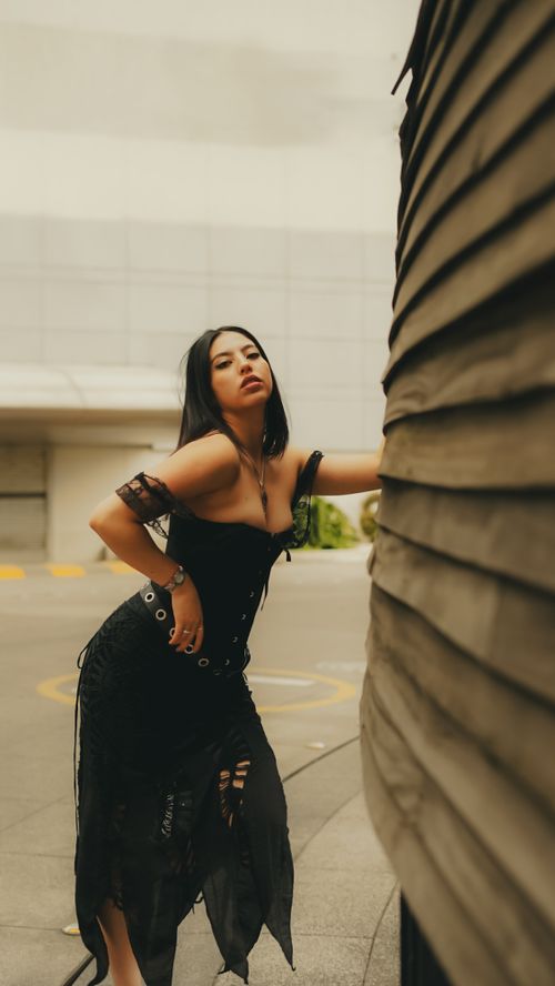 Free Stylish woman in black dress posing confidently against textured wall in urban environment. Stock Photo