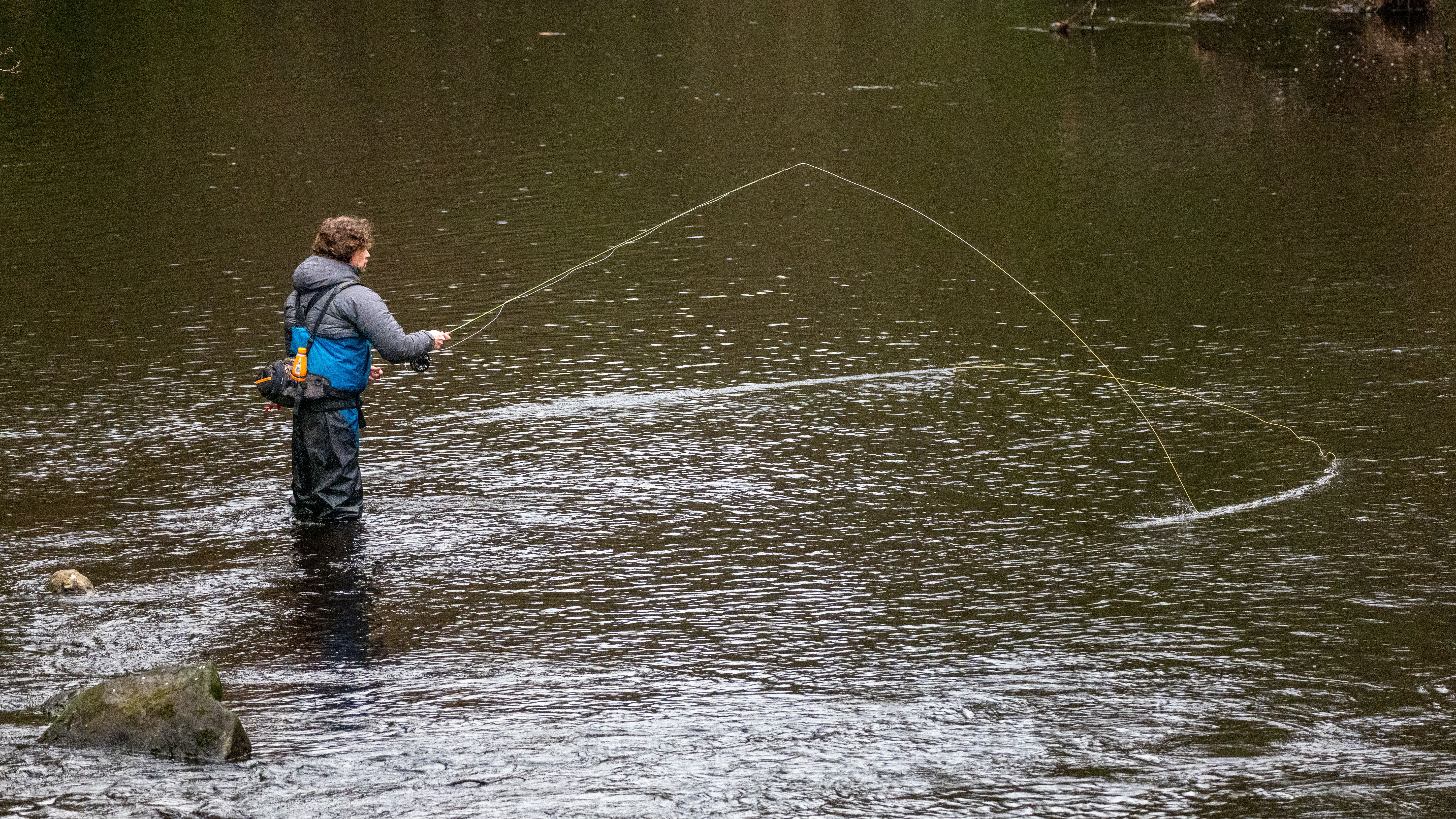 A fly fisherman casting a line across a river