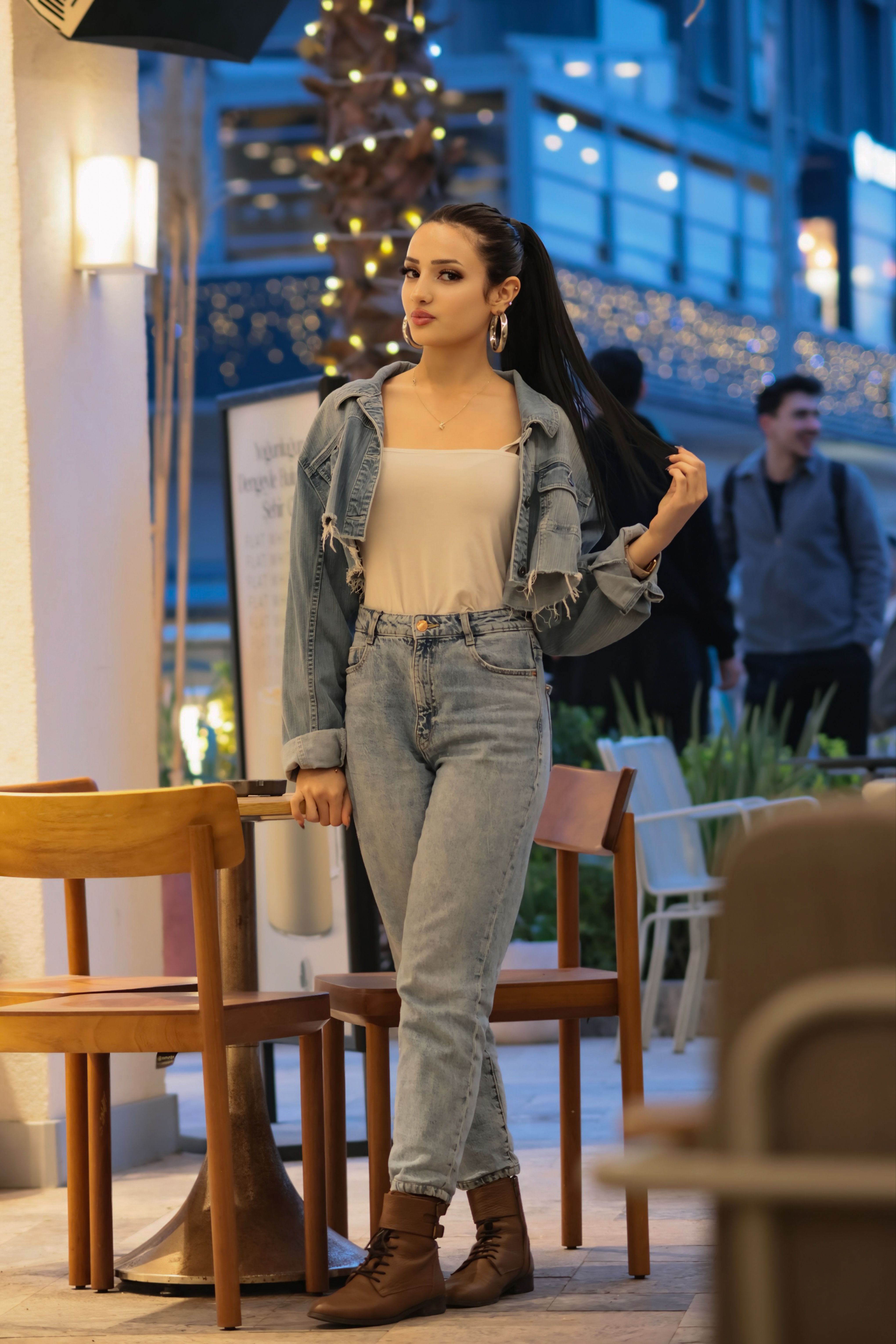 Trendy woman in denim relaxing at a chic outdoor cafe in the city at twilight.