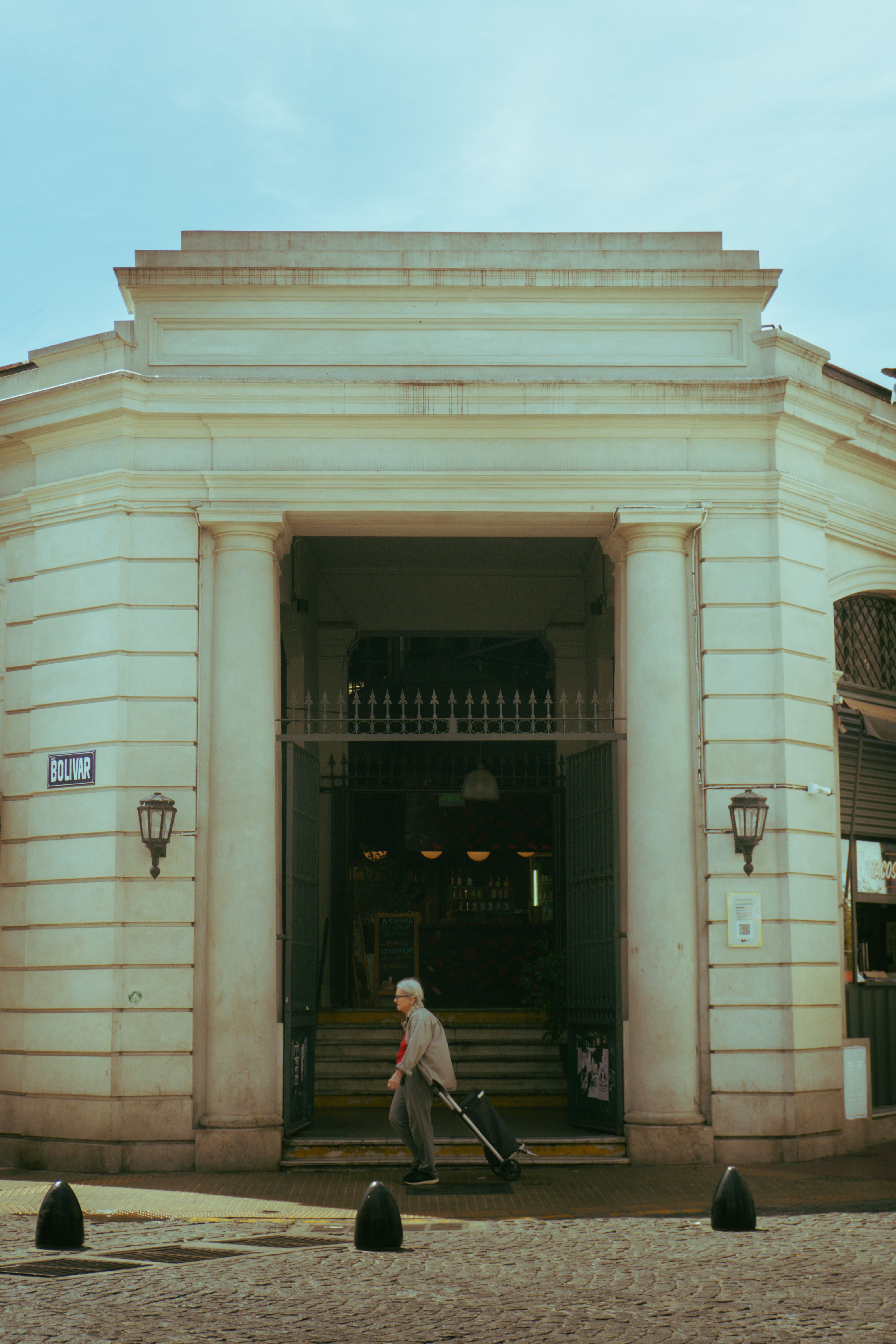 A senior adult walks with a trolley by the entrance of San Telmo Market, showcasing its architecture.