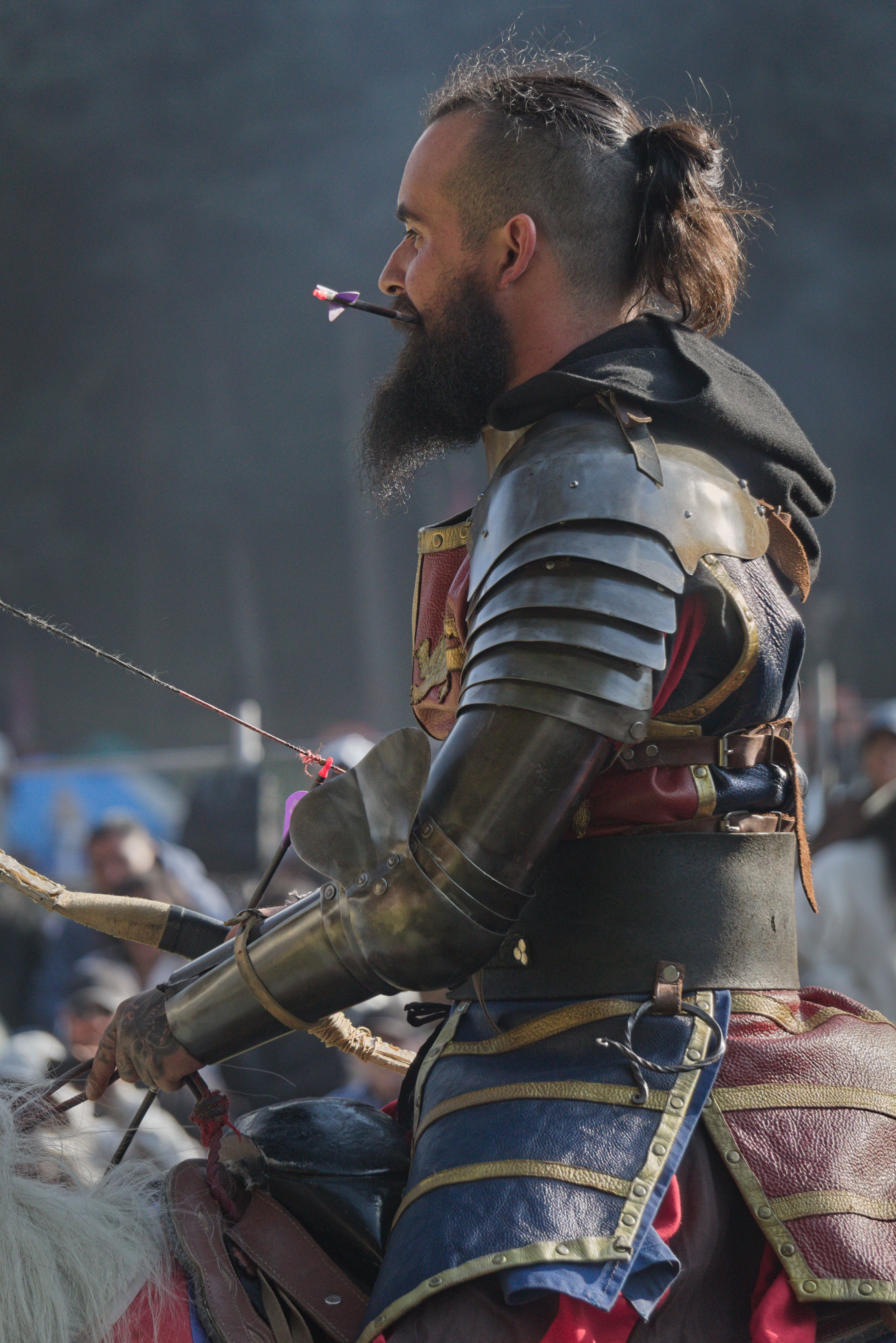 A medieval reenactor in full armor riding a horse during a historical event outdoors.