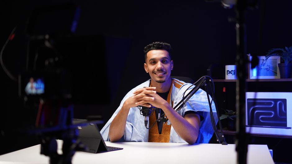 Podcaster in a studio setting, speaking into a professional microphone with a tech-savvy backdrop.
