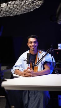 A smiling young man in a studio recording a podcast with professional equipment.