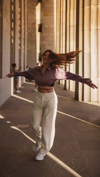 A woman joyfully twirls in a sunny, architectural corridor. Captured beautifully with warm tones.